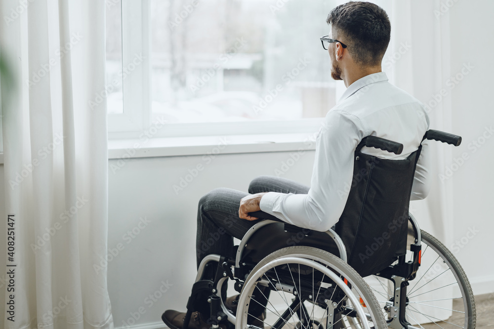 Young disabled man sitting in a wheelchair near the window Young disabled man sitting in a wheelchair near the window