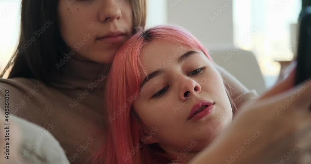 Gay woman using mobile phone with girlfriend lying on sofa at home Gay woman using mobile phone with girlfriend lying on sofa at home