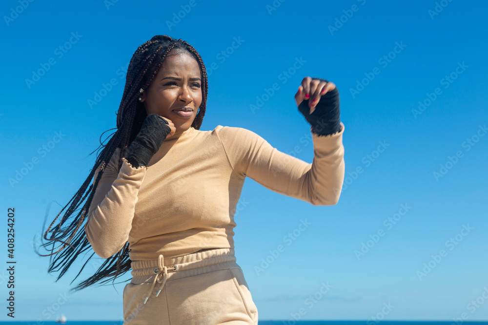 Young afro black girl training martial arts, boxing outdoors with sea and blue sky background. Attitude, sport, workout. Young afro black girl training martial arts, boxing outdoors with sea and blue sky background. Attitude, sport, workout.