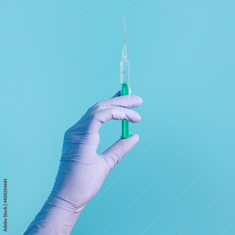 Syringe for injection in hand, latex medical gloves on hand. On a blue background. Syringe for injection in hand, latex medical gloves on hand. On a blue background.