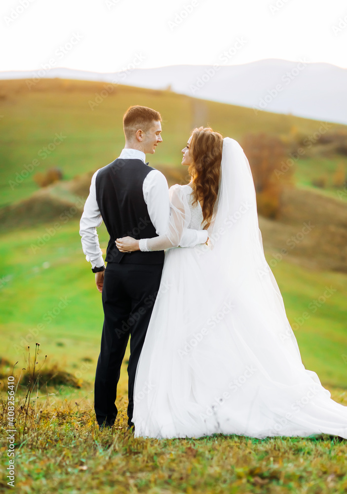 A loving couple wedding newlyweds in a white dress and a suit walking on the mountain backround, sunset.