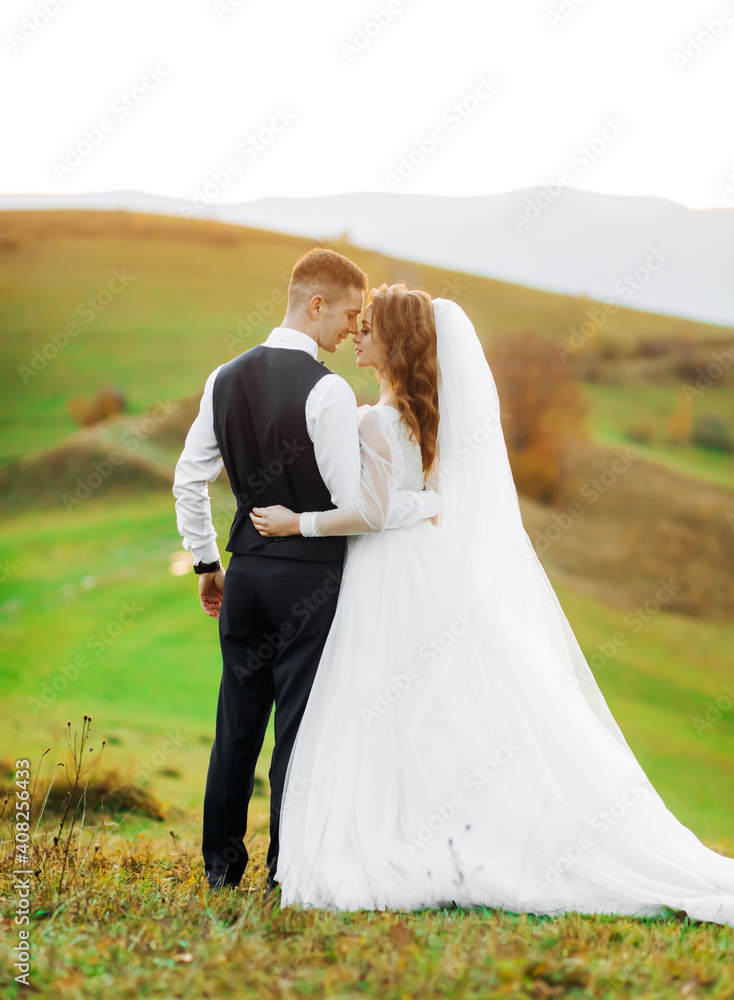 Wedding couple standing and embracing on a hill meadow and enjoys the view of the summer sunset. A mountain hill. Amazing landscape.