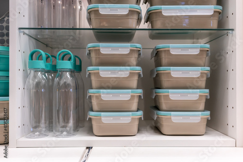 Stack of plastic food containers and black clear plastic bottles inside white cabinet.