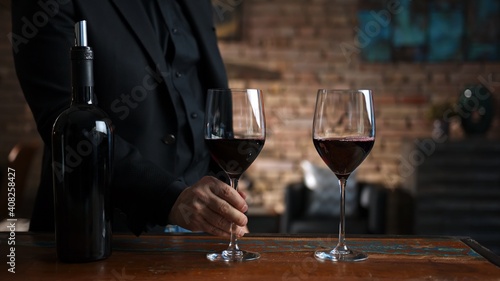 Elegant man tasting and serving red wine in a couple of wine glasses at home in a cosy dark room.