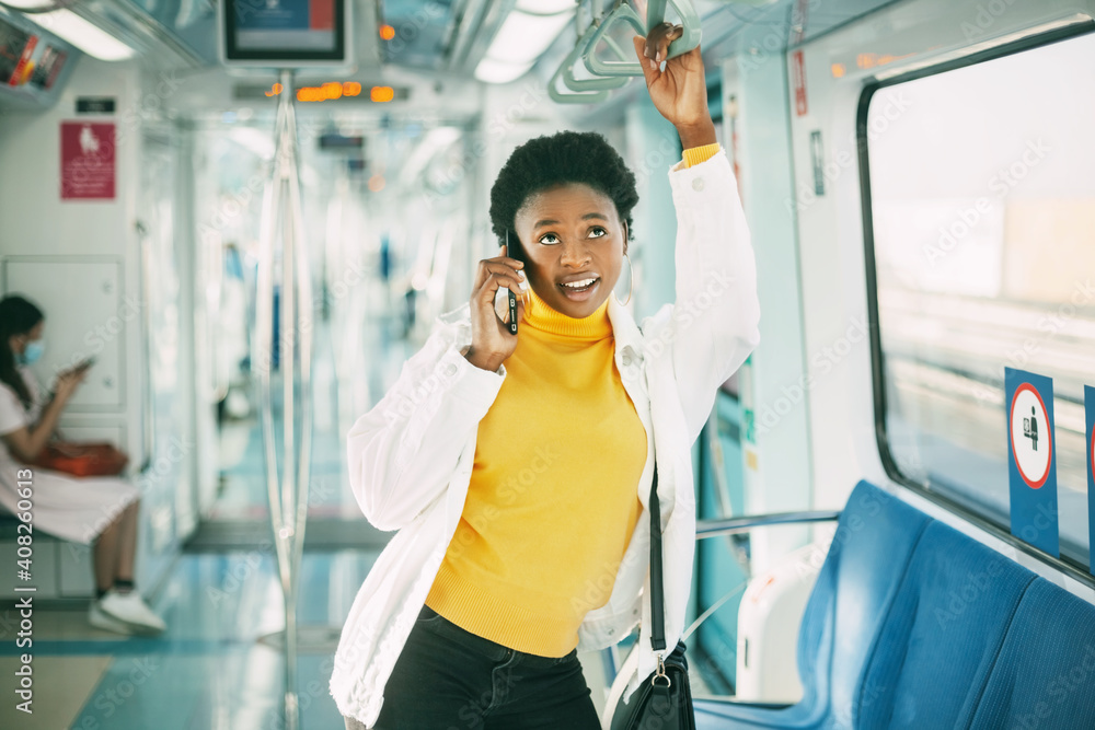 Smiling young African woman holding on to the railing and talking on the phone, standing in the subway train during your daily commute Smiling young African woman holding on to the railing and talking on the phone, standing in the subway train during your daily commute