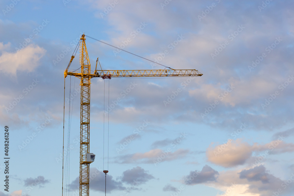 Metal structure construction crane on the background of the sunset sky with clouds