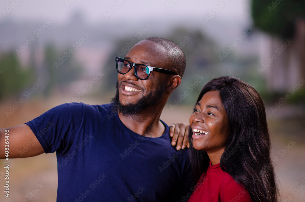 Naklejka premium young african man and woman standing outside and delighted while using a smart phone to take a picture
