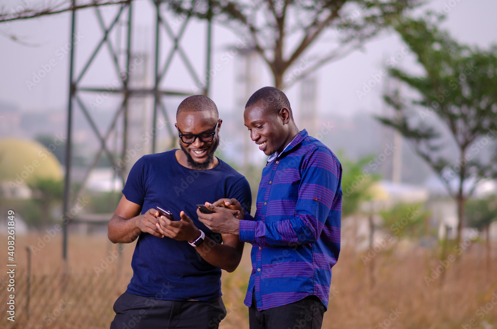 young african men standing outside and delighted while using their smart phones young african men standing outside and delighted while using their smart phones
