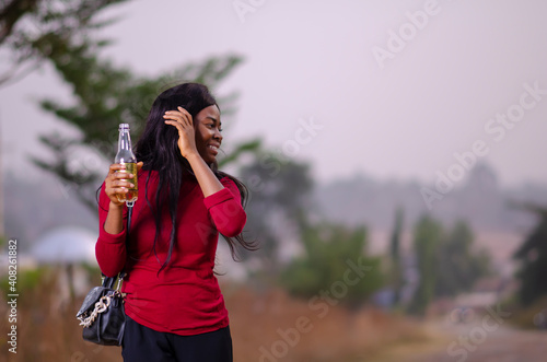 young beautiful african lady standing in a garden and holding a bottle of drink © Courage