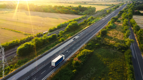 Aerial Drone Shot: Long Haul Semi Trucks Driving on the Busy Highway in the Rural Region of Italy. Agricultural Crop Fields and Hills in the Background