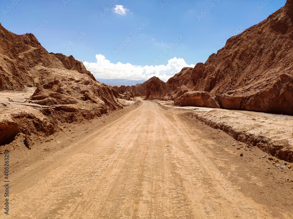 Endless sandy road surrounded by rough rocks under blue sky on sunny day in Atacama desert