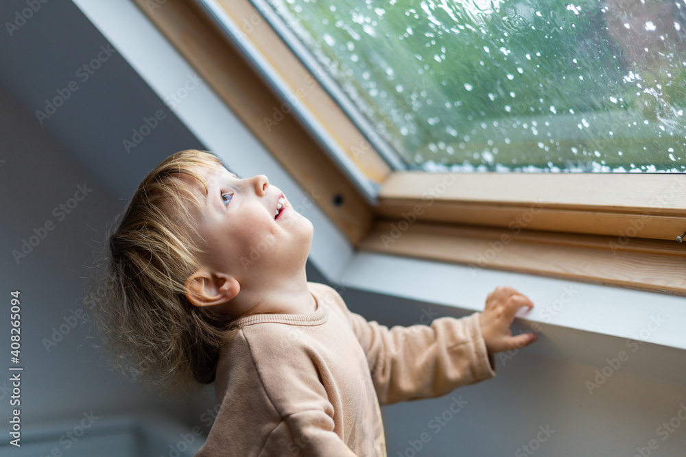 Little preschool boy staying home in bad weather and looking with interest through window on raindrops and hail, idoors. Little preschool boy staying home in bad weather and looking with interest through window on raindrops and hail, idoors.