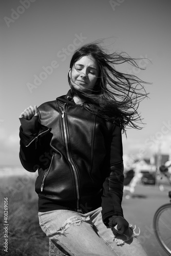 Portrait of a young beautiful girl with closed eyes, in leather jacket, by the sea and feel cold.