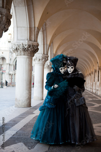 Masked couple in ornate costume at the the Venetian masquerade stands against stone wall near St. Mark's Square in Venice