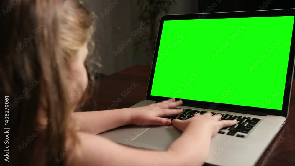 Over the shoulder little girl use laptop with green screen mock-up template on a display. Close-up shot typing on notebook keyboard. Computer online e-learning Over the shoulder little girl use laptop with green screen mock-up template on a display. Close-up shot typing on notebook keyboard. Computer online e-learning