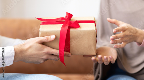 Male Hands Giving Gift Box To Muslim Wife Indoors, Closeup