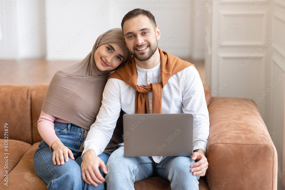 Happy Muslim Couple Sitting With Laptop Hugging Posing At Home Happy Muslim Couple Sitting With Laptop Hugging Posing At Home