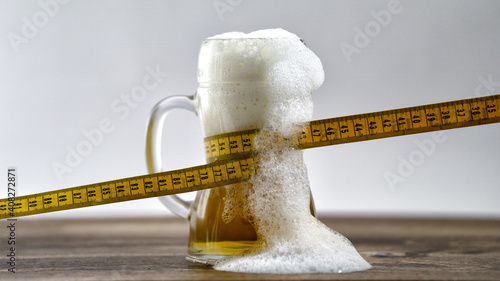 Tape measure wrapped around a glass of fresh draught beer. Diet weight loss concept bad habit beer belly obesity alcohol addict