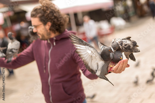 Man feeding pigeons on city square while traveling on vacation