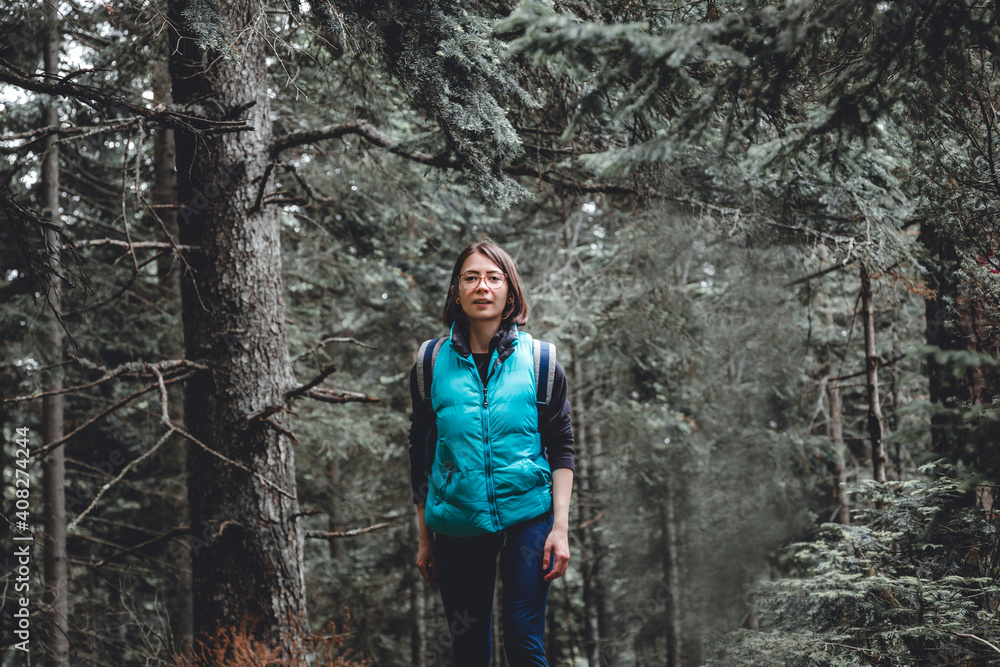 Obraz premium Young woman hiking through an evergreen forest in the mountains