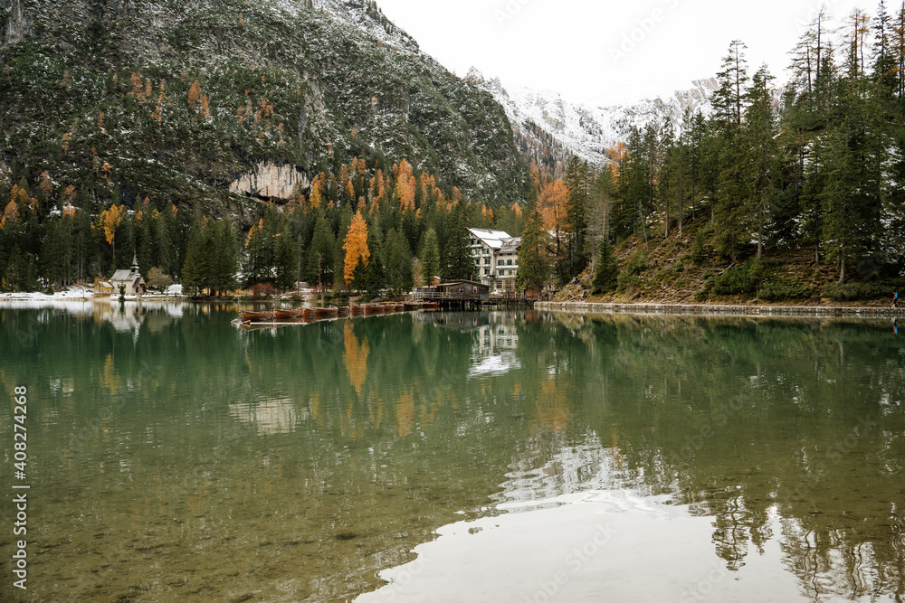 snowy landscape with mountains, trees, boats to navigate in the water in the lago di braies. Located in the dolomites, the Italian alps