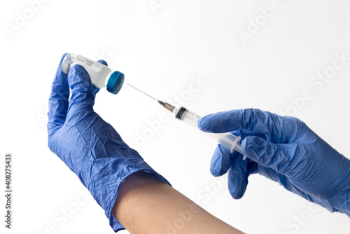 Close up of hands in blu medical gloves holding syringe and  bottle with vaccine on  light background. Preventive COVID-19 vaccination , coronavirus concept