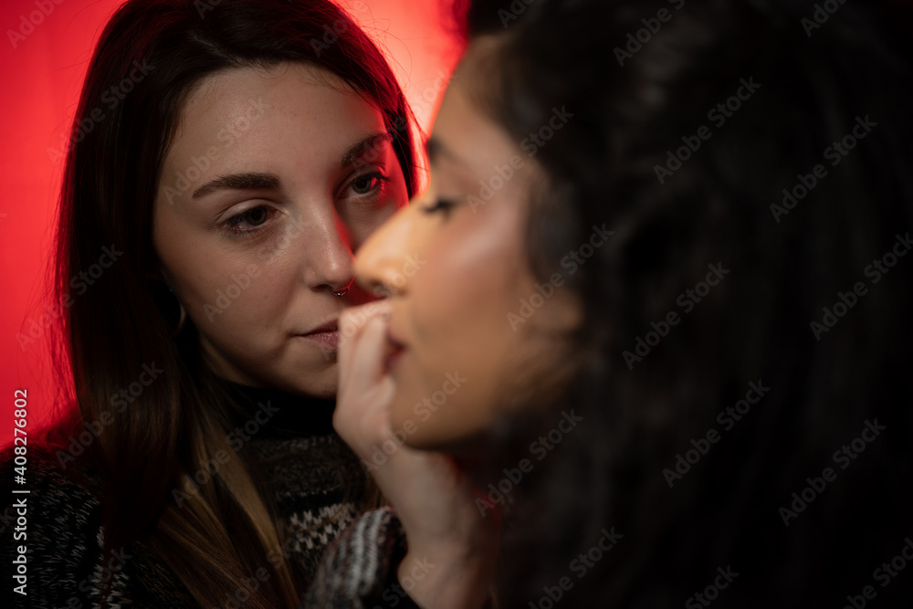 Maquilladora profesional maquillando a una modelo de piel morena, iluminada por una luz roja.
