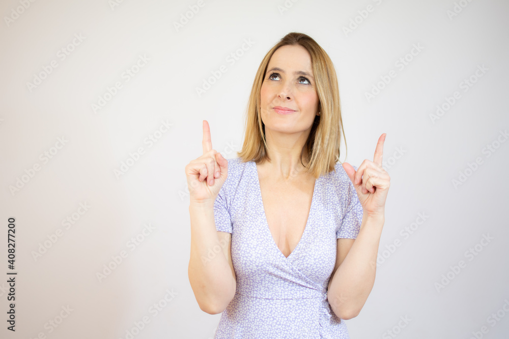 Young woman pointing up with both index fingers while smiling cheerfully away, standing over white background. Young woman pointing up with both index fingers while smiling cheerfully away, standing over white background.
