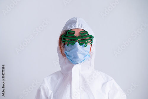 A woman in a protective suit and a medical mask and wearing funny glasses celebrates st patrick's day photo