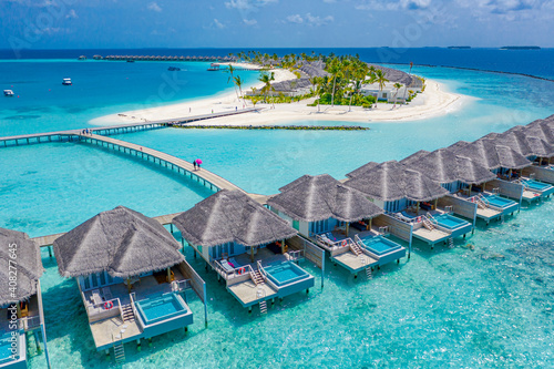 Aerial view of Maldives island, luxury water villas resort and wooden pier. Beautiful sky and ocean lagoon beach background. Summer vacation holiday and travel concept. Paradise aerial landscape pano © icemanphotos