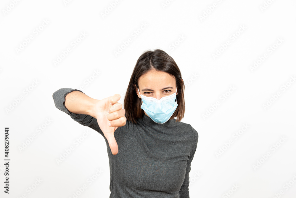 Disgusted latin woman wearing a face mask with the thumbs down. Mental health during Coronavirus pandemic concept. Disgusted latin woman wearing a face mask with the thumbs down. Mental health during Coronavirus pandemic concept.