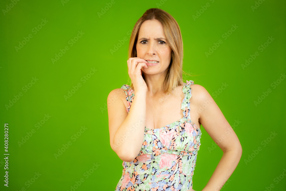 Fototapeta premium Young beautiful blonde woman wearing casual dress over green isolated background Thinking worried about a question, concerned and nervous with hand on mouth