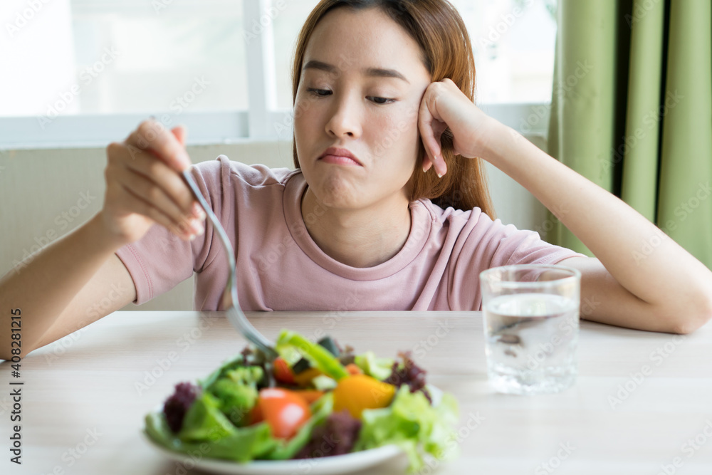 unhappy asian women is on dieting time looking at broccoli on the fork. girl do not want to eat vegetables and dislike taste of vegetable. unhappy asian women is on dieting time looking at broccoli on the fork. girl do not want to eat vegetables and dislike taste of vegetable.