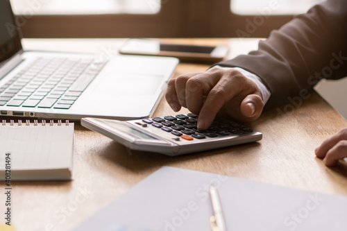 Businessman counting on calculator and reviewing budget on business plan.