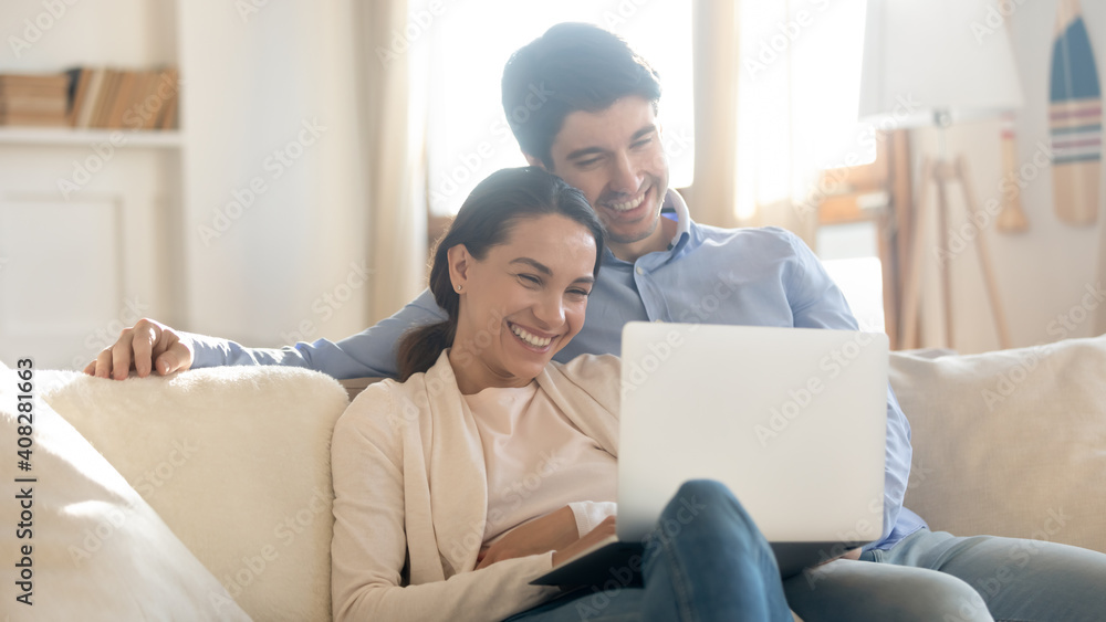 Close up overjoyed couple looking at laptop screen, sitting on cozy couch at home, smiling woman and man hugging, using computer, booking or shopping online, enjoying leisure time with device Close up overjoyed couple looking at laptop screen, sitting on cozy couch at home, smiling woman and man hugging, using computer, booking or shopping online, enjoying leisure time with device