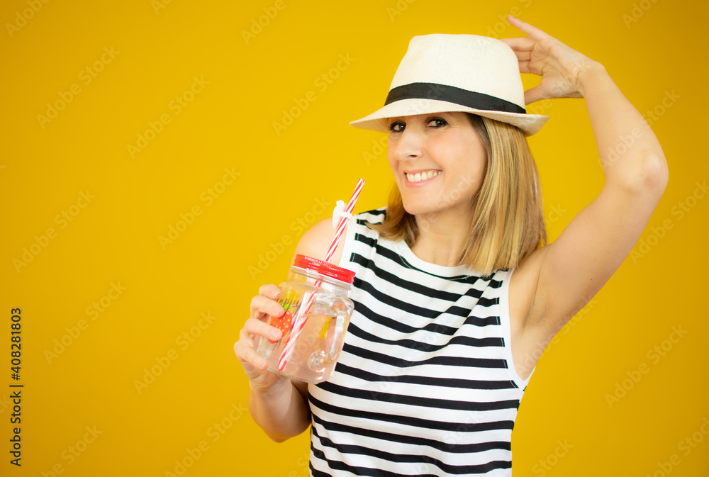 Smiling woman wearing straw hat holding orange juice glass over yellow background. Smiling woman wearing straw hat holding orange juice glass over yellow background.