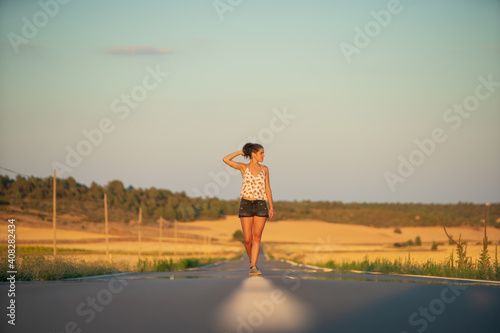 Young girl, walking in the middle of a lonely straight road, late in the day.
