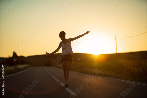 Young girl  walking in the middle of a lonely straight road  late in the day. With the hands stretched out in the shape of a cross  to maintain balance and not fall from the dividing line.