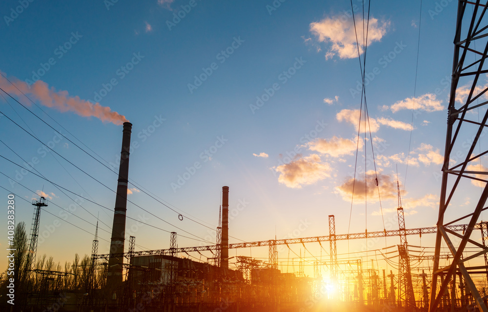 A silhouette of thermal power station and high voltage power lines against a colorful sky at sunrise. A silhouette of thermal power station and high voltage power lines against a colorful sky at sunrise.