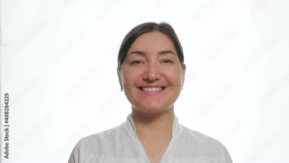 Nice young woman with dark hair wearing trendy white shirt smiles gently posing for camera on professional studio background close view Nice young woman with dark hair wearing trendy white shirt smiles gently posing for camera on professional studio background close view