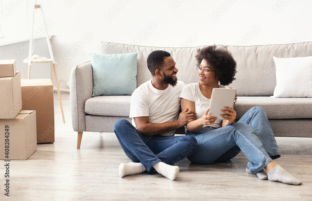 Black Couple Using Tablet Sitting Indoors, Among Moving Boxes