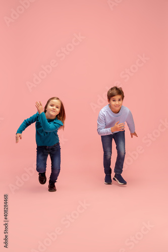 Aspiration. Happy children isolated on coral pink studio background. Look happy, cheerful. Copyspace for ad. Childhood, education, emotions, facial expression concept. Having fun, running on