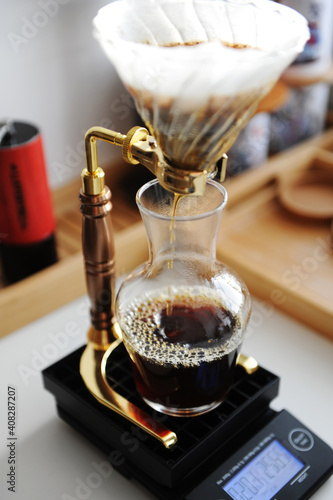 Pour over coffee brewing on gold drip stand. Glass dripper and carafe, black scales