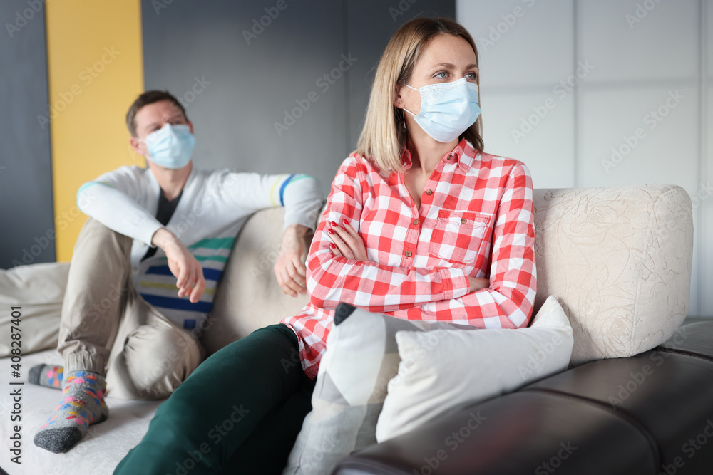 Offended woman and man are sitting on couch wearing protective masks