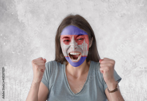 Young woman with painted flag of Cambodia and open mouth looking energetic with fists up