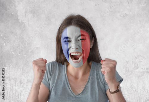 Young woman with painted flag of France and open mouth looking energetic with fists up photo