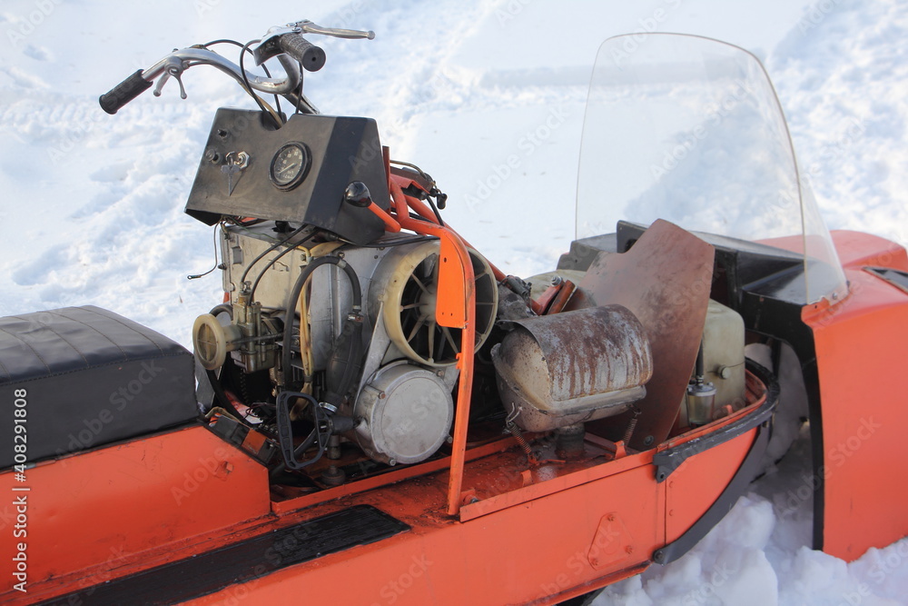 Old Russian utility snowmobile without hood close up - dashboard with control panel and ignition key, steering, air cooled engine with emergency start handle and fuel tank