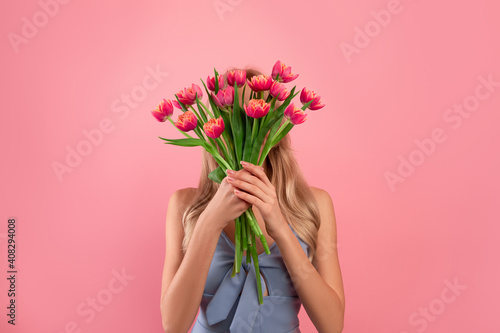 Flowers for special occasion. Anonymous young lady holding bouquet of tulips in front of her face over pink background