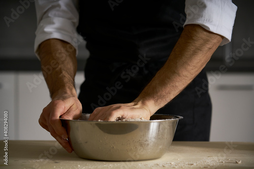 The hands of the strong man knead the dough from which they will make bread, pasta, cake or pizza. In his kitchen he carries on the tradition of homemade pasta. A cloud of white flour flies like dust.