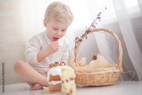 The kid eating traditional russian easter cake on table. The decorarion of kulich are the flower are cooking for spring holiday photo